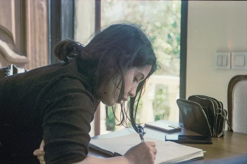 A woman leaning over a table, writing in a notebook.
